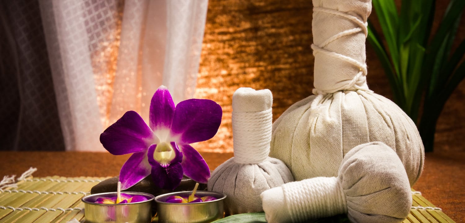 Spa herbal compressing ball with candles and orchid on brown background.